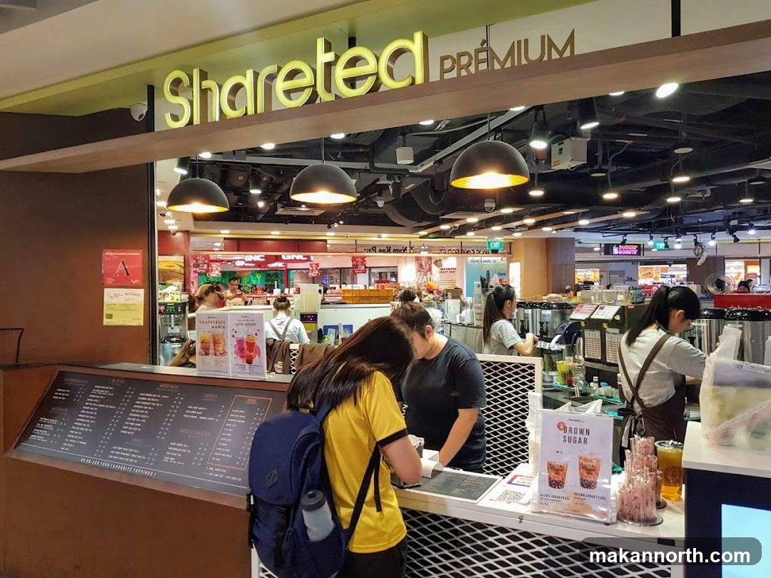 A view of the Sharetea Premium storefront with staff preparing drinks behind the counter. A menu board is visible in the foreground.