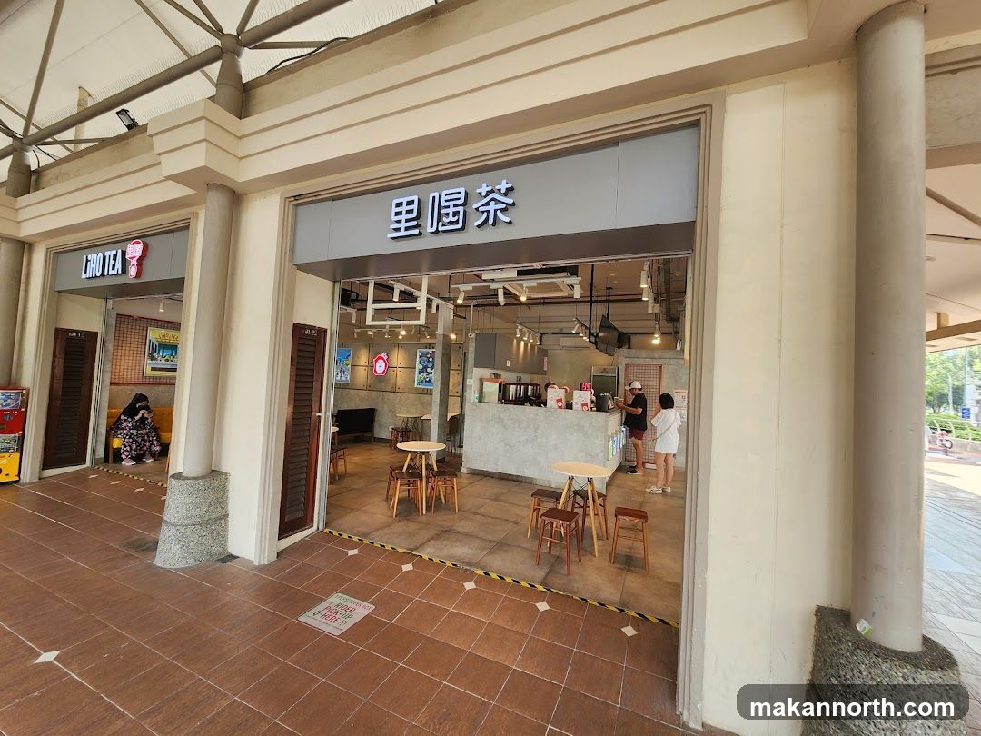 The exterior of a tea shop with a prominent sign above the entrance. Inside, there are tables and chairs, a counter, and customers. Another shop,