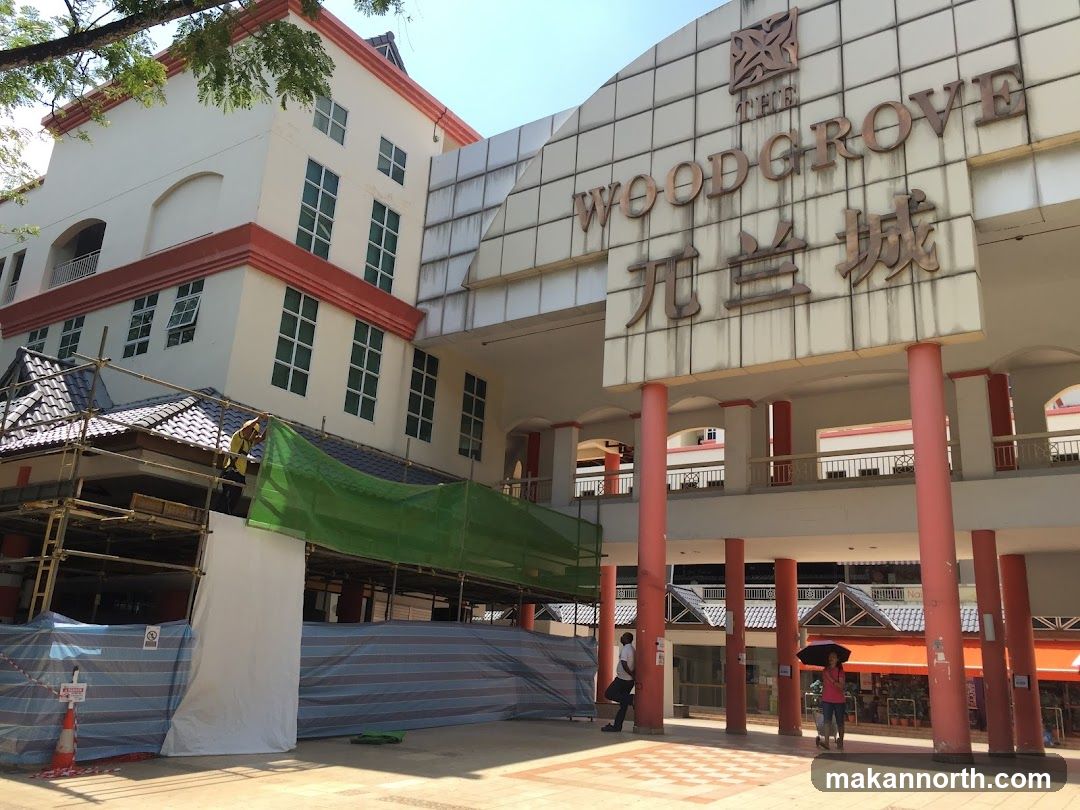 The exterior of The Woodgrove building, with scaffolding and tarps covering a section of the lower level. The building has a large sign with the name "THE WOODGROVE" in English and Chinese characters.