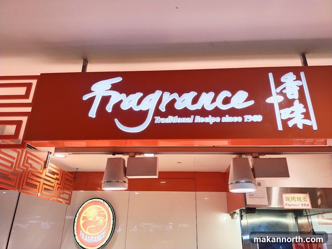 A bright orange sign with white illuminated text reads "Fragrance Traditional Recipe since 1969" and Chinese characters. Below the sign, there are lights and a circular logo with the word "FRAGRANCE" inside. A sign that says "FRESHLY BBQ" is also visible.