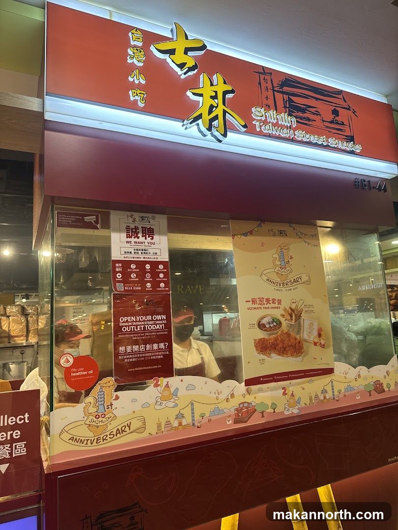 A red and white storefront for Shihlin Taiwan Street Snacks. The sign above the storefront reads "台灣小吃" and "Shihlin Taiwan Street Snacks". There are two employees visible behind the glass counter. A poster advertises an anniversary special.