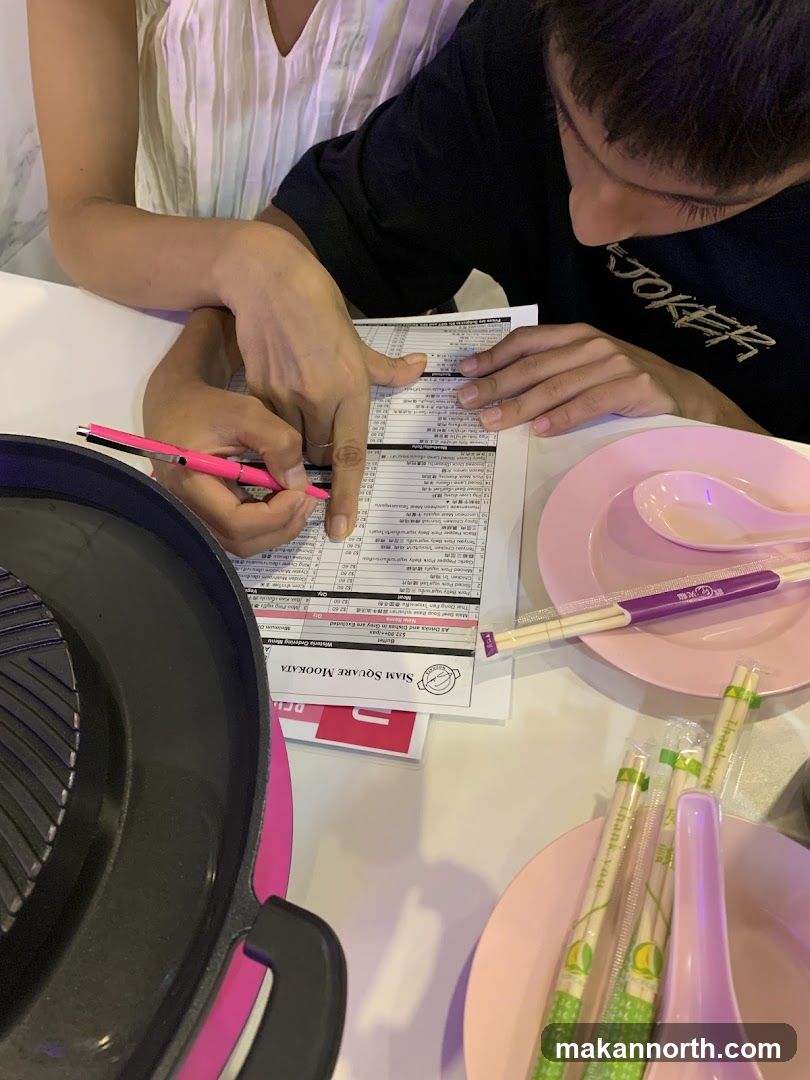 Two people are looking at a menu at a table. There is a pink grill in the foreground.