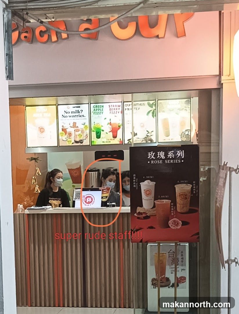 A counter at a bubble tea shop with staff members wearing masks. There are illuminated menu boards displaying drinks like "No milk? No worries.", "Green Apple Fizzy", "Strawberry Fizzy", and "Osmanthus Milk Tea". A poster for the "Rose Series" is also visible, showing different cup sizes and prices. A small screen on the counter displays a logo. Text on the image reads "super rude staff!!!!".