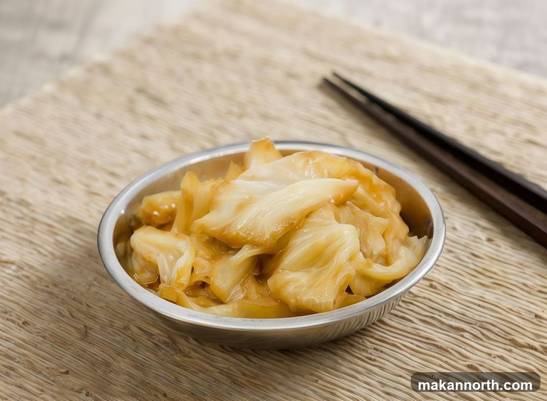 A small metal bowl filled with braised cabbage sits on a woven placemat. A pair of dark chopsticks rests to the right of the bowl.