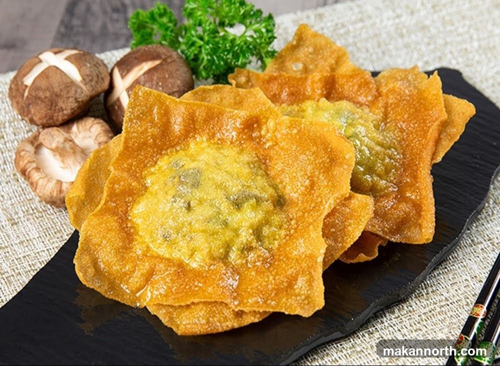 A close-up shot of golden-brown fried wontons, filled with a green mixture, arranged on a black slate plate. Several shiitake mushrooms and a sprig of parsley are visible in the background. Chopsticks rest on the right side of the plate.