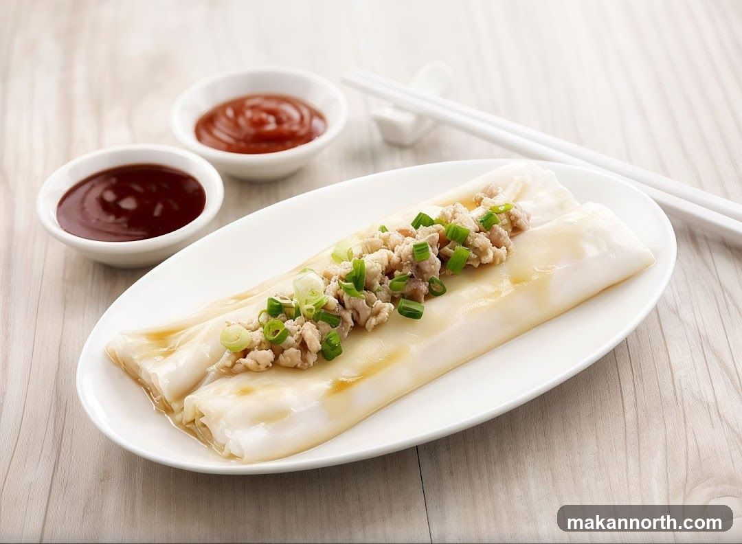 A close-up shot of two steamed rice rolls, also known as cheung fun, topped with minced pork and chopped scallions. The rolls are served on a white oval plate with two small white bowls of dipping sauce and a pair of white chopsticks resting on a chopstick rest in the background. The plate and sauces are placed on a light-colored wooden surface.