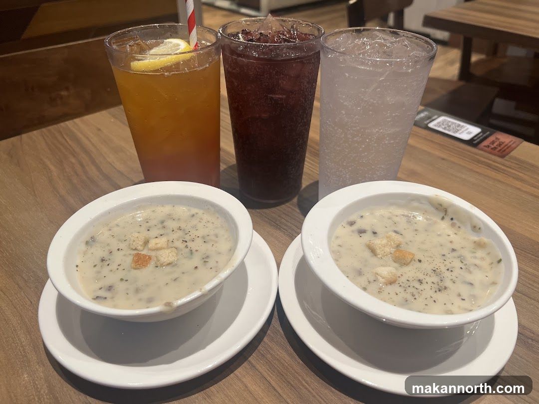 Two bowls of creamy mushroom soup with croutons and three drinks on a wooden table.
