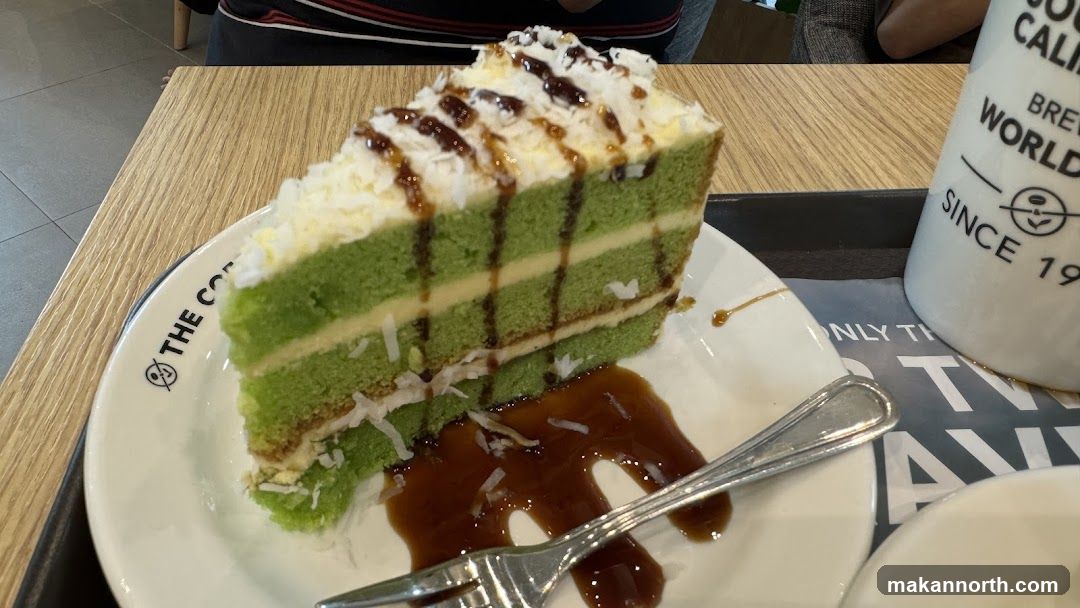 Slice of green cake with white frosting and chocolate drizzle