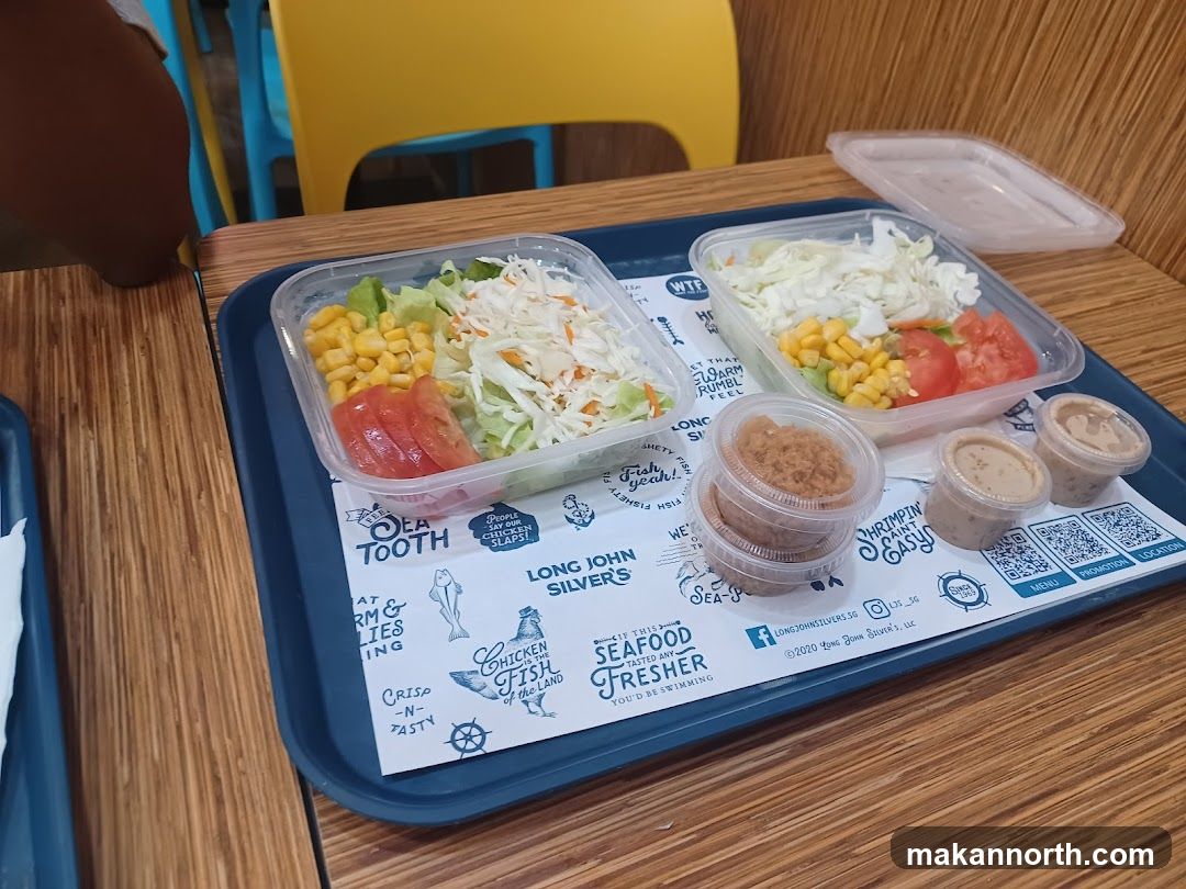 Two salads with corn, tomatoes, and shredded cabbage, served with small containers of sauce and shredded meat.