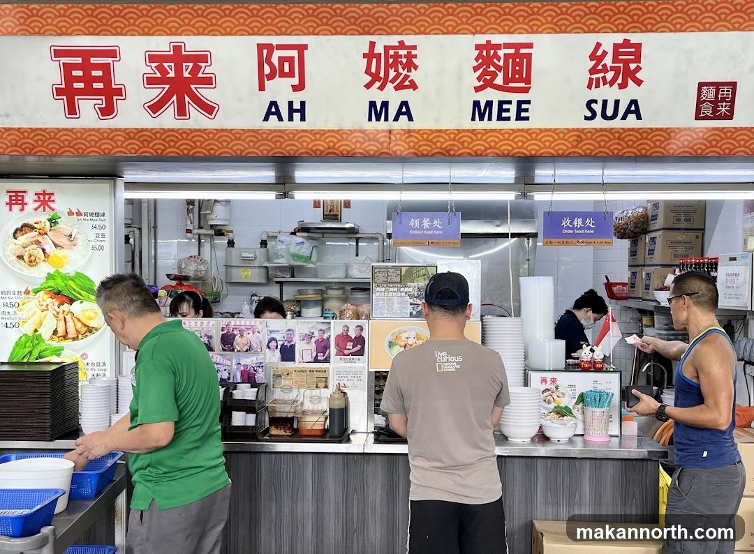 A food stall with a large sign above that reads "再来阿嬤麵線" (Ah Ma Mee Sua). There are menus displayed on the left side of the stall, showing dishes like "妈妈生" and "肉丸汤" for $4.50. Customers are seen ordering and collecting food.