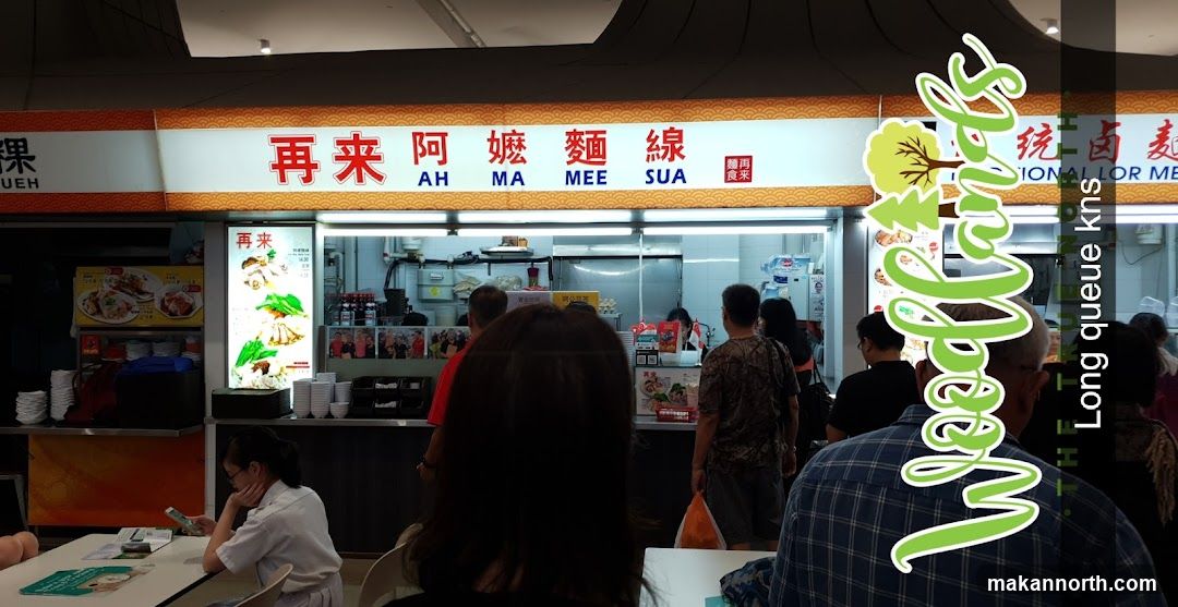 A food stall with a sign that reads "再来阿嬤麵線" (Zai Lai Ah Ma Mee Sua) and "AH MA MEE SUA". There are pictures of food displayed and people queuing.