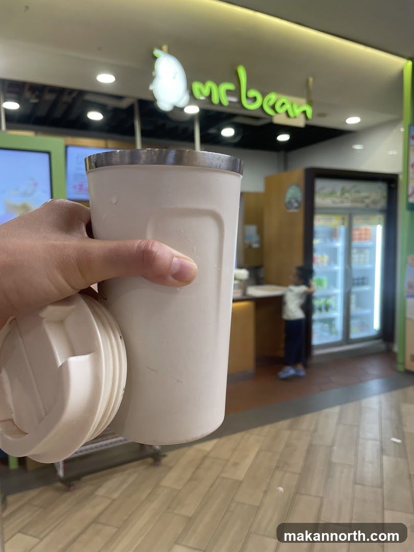 Person holding a reusable cup in front of a Mr. Bean store
